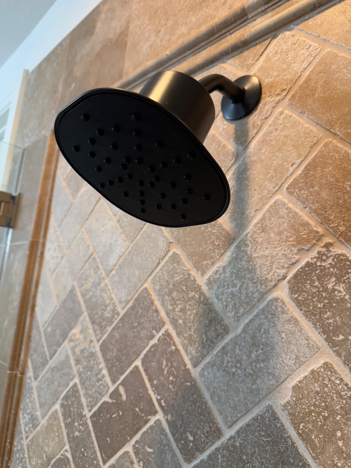Matte black Afina filtered shower head installed on a stone tile shower wall, blending function with style.